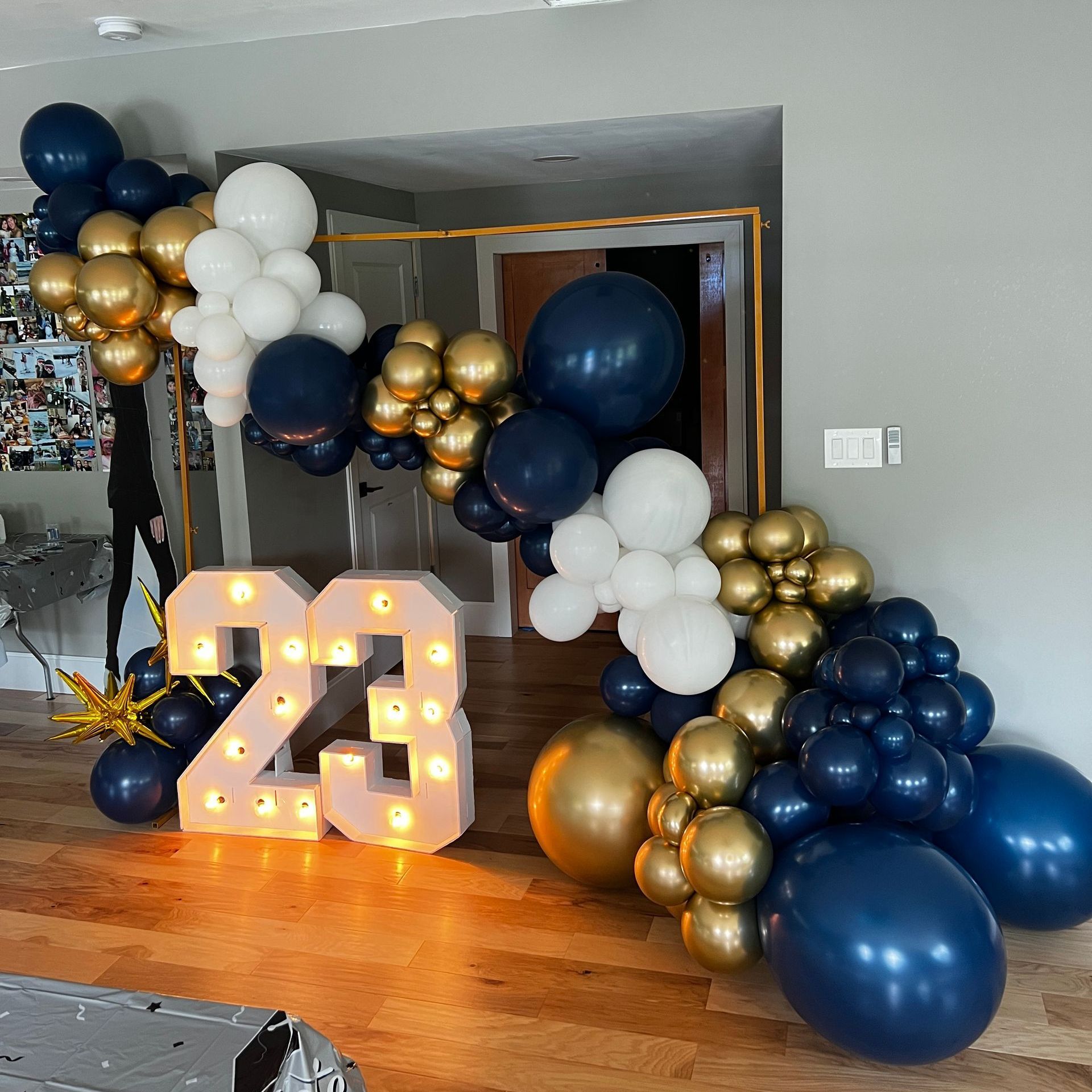 Chrome navy blue, chrome gold, and white grand deluxe balloon garland on a square frame, creating a unique and stylish look. Paired with '23' LED marquee lights, perfect for indoor or outdoor balloon decorations for graduation or celebratory events.