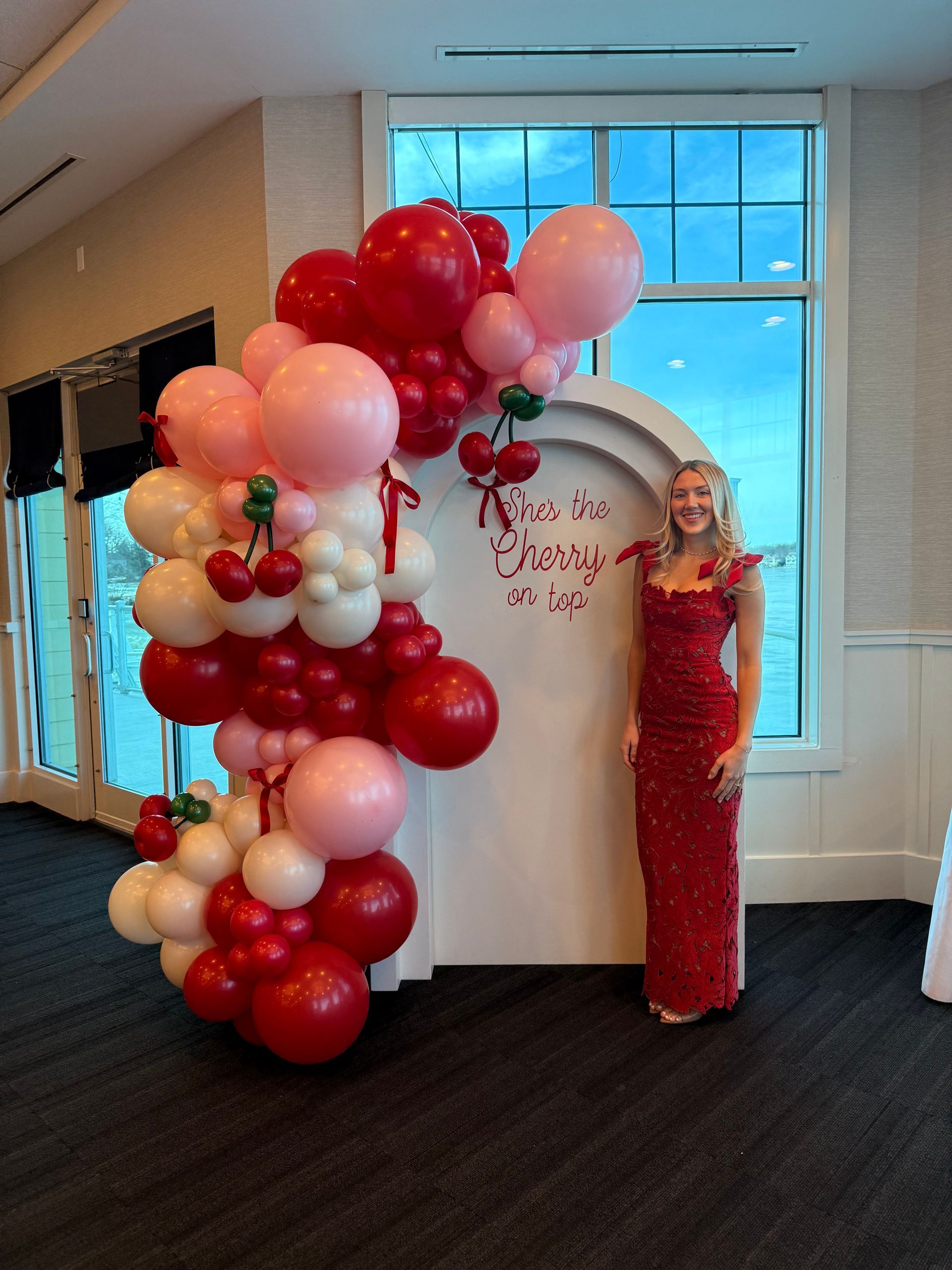 'She's the Cherry on Top' themed bridal shower at the Lakes of the Four Season's Clubhouse featuring a red, matte pink, and pearl deluxe luxury balloon garland paired with a tiered arch wall adorned with custom vinyl. Accented with red bow ties for a playful and elegant touch.
