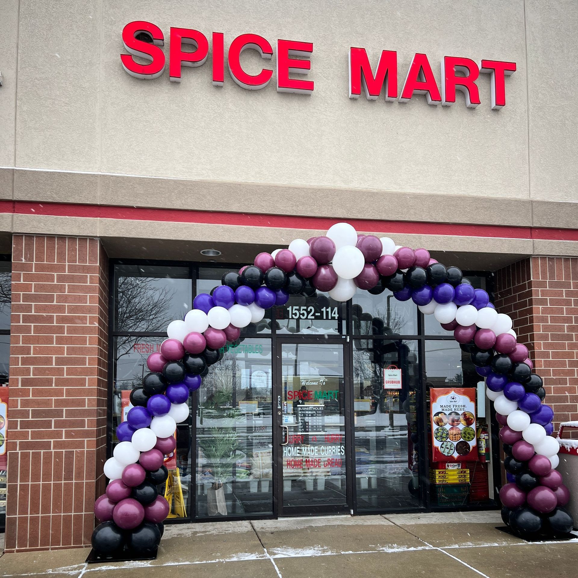 Deluxe double spiral balloon arch for Spice Mart's grand opening in Naperville, IL, featuring shades of purple and white. A vibrant and eye-catching entrance decor that adds a festive touch to the event, making it a memorable celebration.