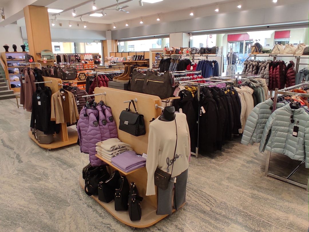 Interno di un negozio di abbigliamento con appendiabiti e manichini. Sono esposti cappotti, borse e scarpe.