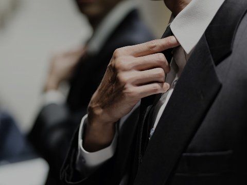 Un uomo in smoking si sistema il colletto, un altro uomo è sfocato sullo sfondo.