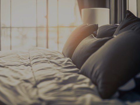 Letto con cuscini scuri, finestra, luce soffusa.