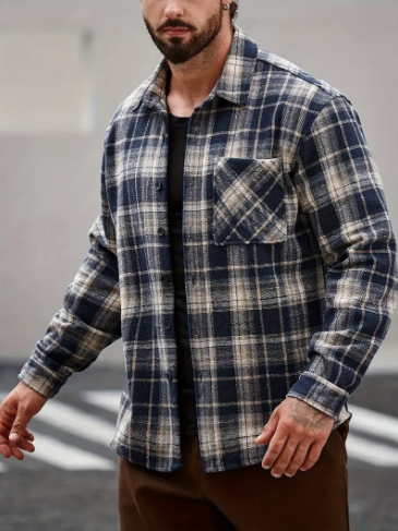 Uomo che indossa una camicia a quadri blu navy e beige sopra una camicia nera, all'aperto.