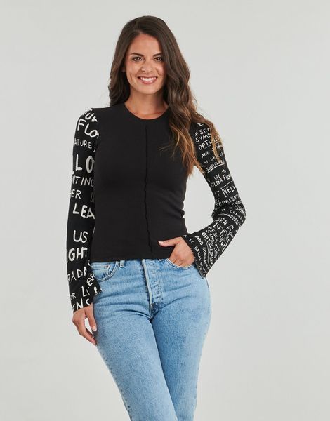 Donna con maglietta nera con scritta sulle maniche, jeans blu, sorridente.