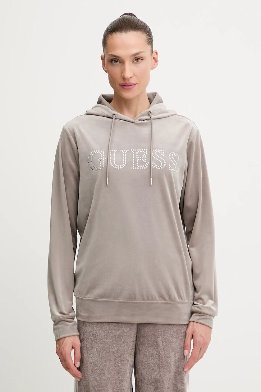 Donna in piedi in un ambiente interno, con indosso una felpa grigia Guess con logo e coulisse.