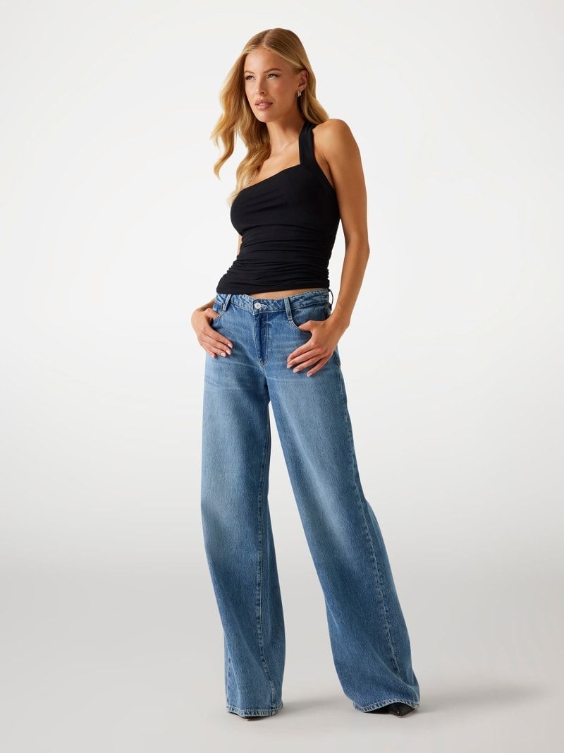Donna in top nero e jeans blu a gamba larga, in piedi con le mani in tasca.
