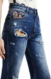 Primo piano di jeans in denim usurati con ricamo sulla tasca e strappo sul ginocchio.