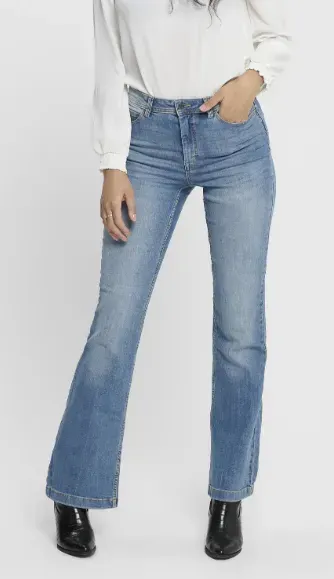 Donna in piedi in uno studio, con indosso jeans svasati azzurri, camicetta bianca e stivaletti neri.