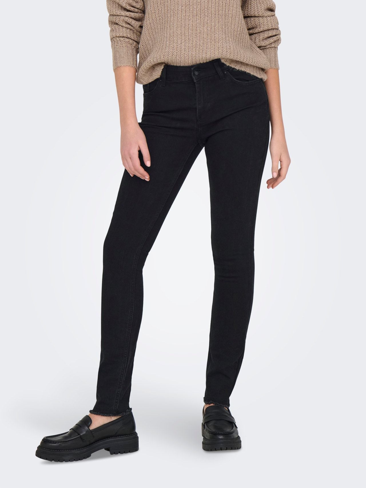 Donna con jeans neri attillati, maglione marrone chiaro e mocassini neri.