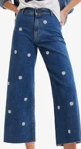 Jeans a gamba larga in denim blu con fiori bianchi ricamati.