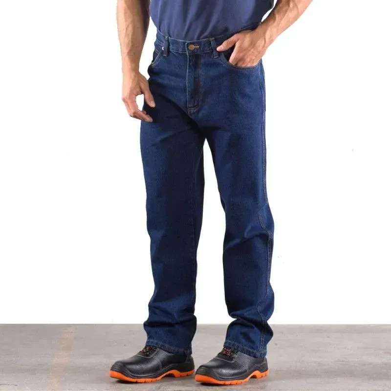 Uomo in jeans, camicia scura e stivali da lavoro, in piedi con una mano in tasca.
