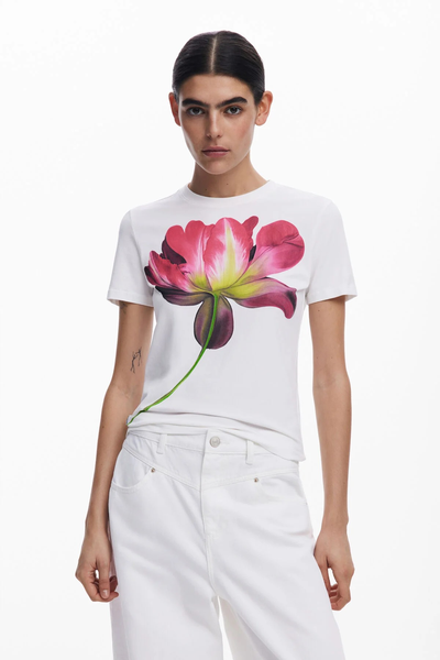Donna con maglietta bianca con grande stampa floreale, abbinata a jeans bianchi.