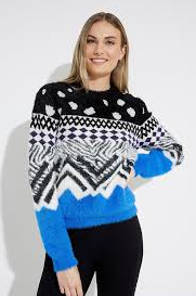Donna sorridente che indossa un maglione con motivi neri, bianchi e blu e pantaloni neri.