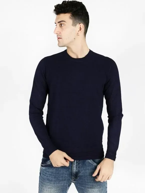 Uomo che indossa un maglione blu scuro e jeans blu, guarda di lato.