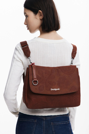 Donna che indossa uno zaino marrone con spallacci regolabili sopra un maglione bianco e jeans blu.