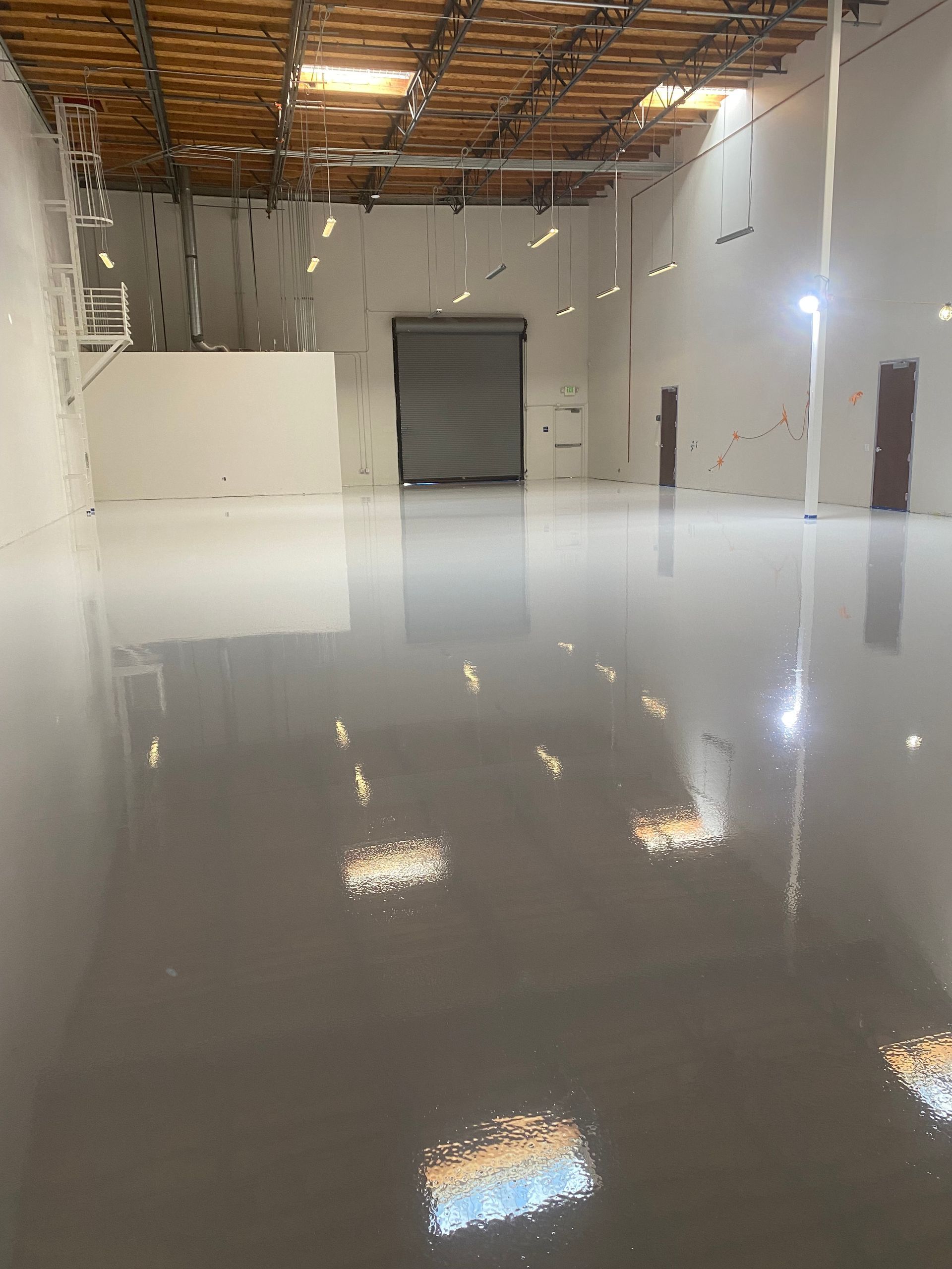 A large empty warehouse with a shiny floor and a garage door.