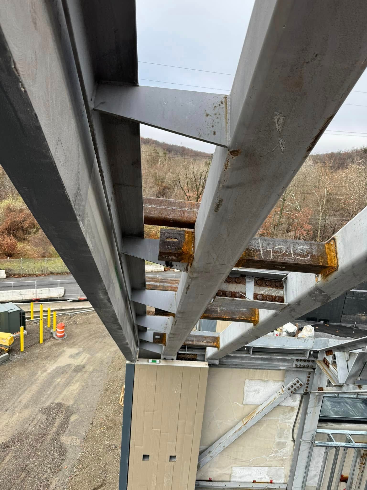 Overhead view of a steel structure, potentially a bridge, with beams and supports. Natural landscape in the background.