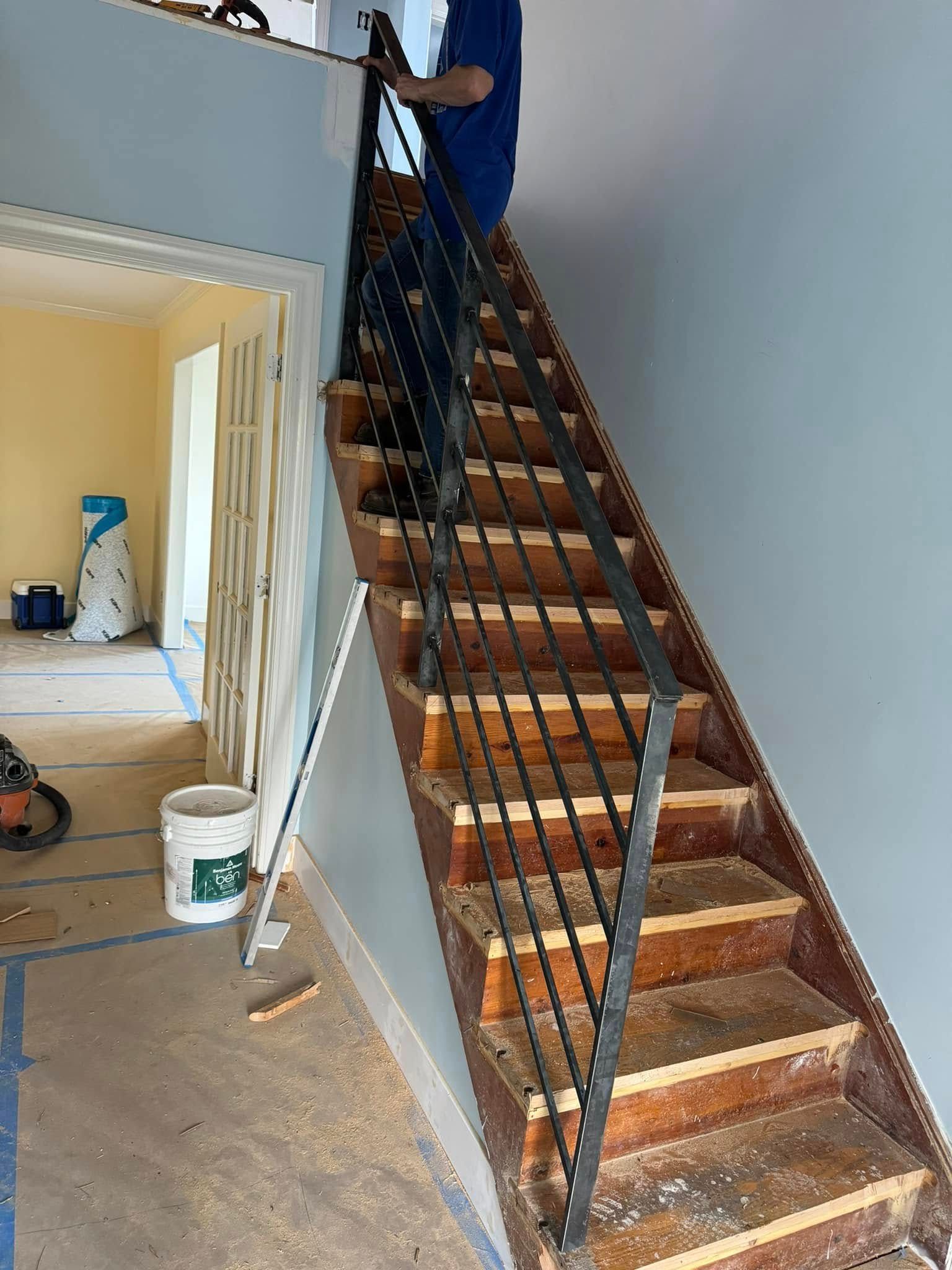 Person on a staircase with metal railing. Wooden steps are worn. Light blue wall. Interior setting.