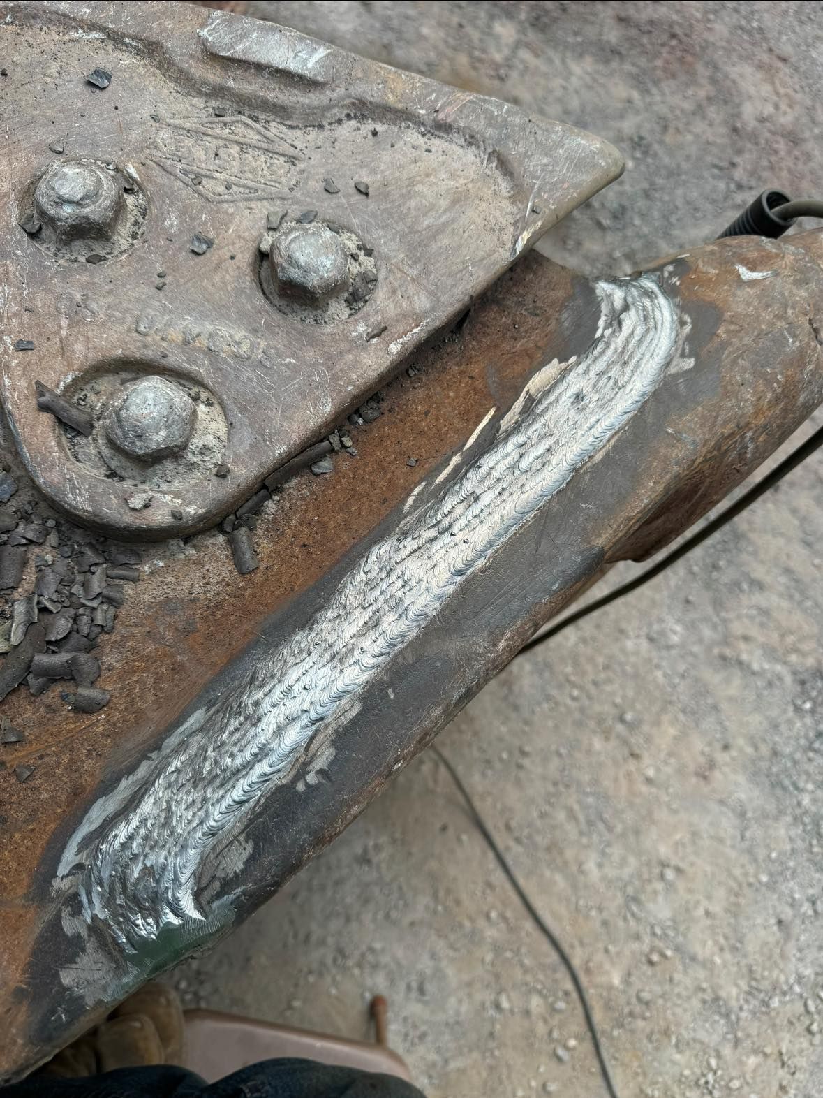 Welded metal joint on a rusted metal structure, showing silver weld marks, bolted metal plate above.