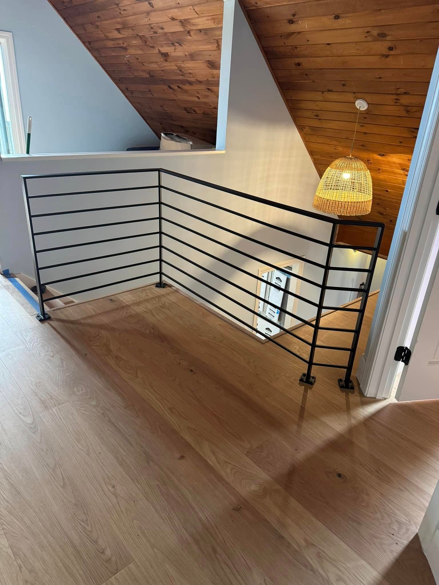 Interior view of a hallway with wooden floors, a black metal railing, and a woven light fixture.