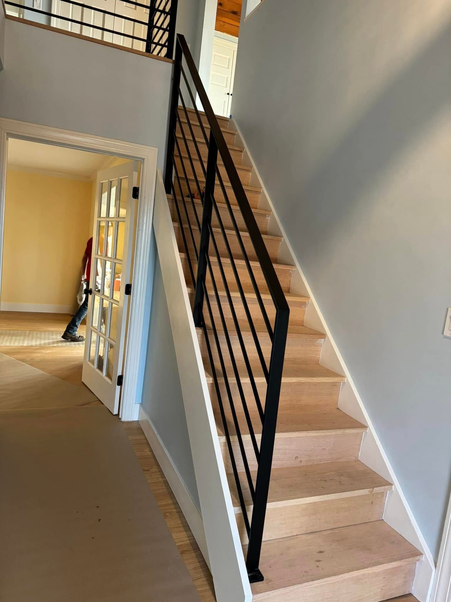Staircase with black railing and light wood steps leading to a second story, light blue walls.