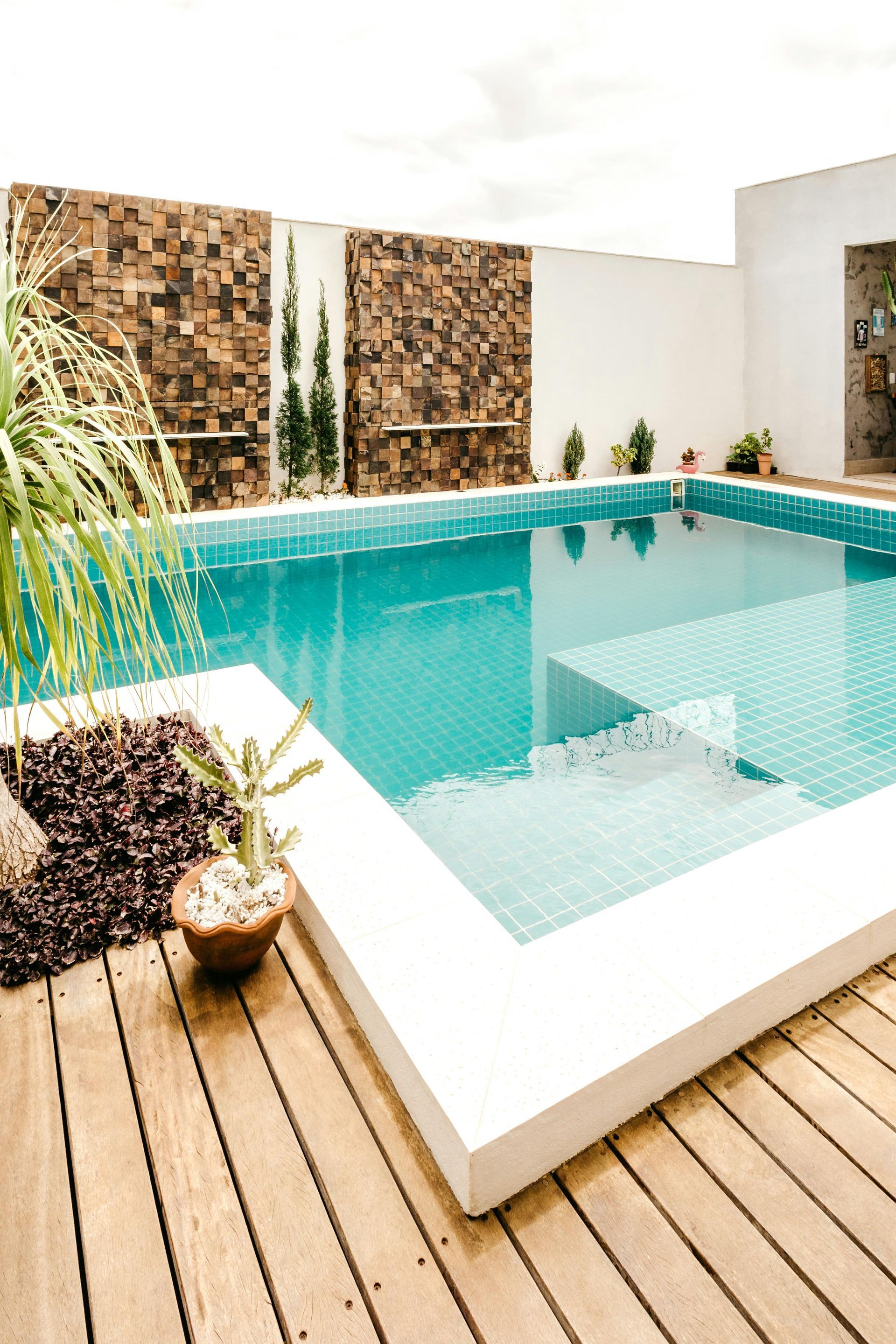 Pool with turquoise water, white edges, wooden deck, and stone accent wall.