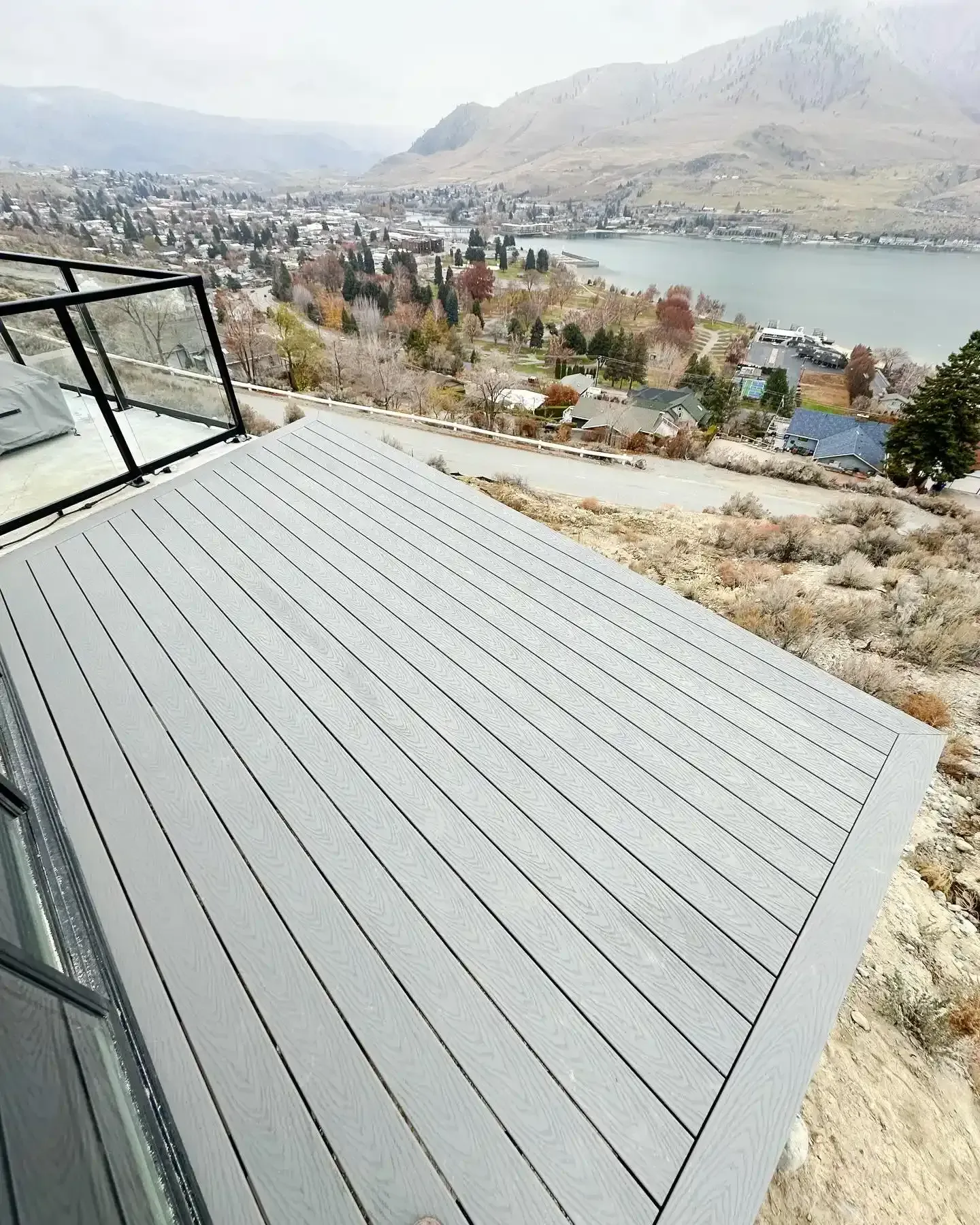 Modern gray deck overlooking a lake, town, and mountains in a scenic hillside view