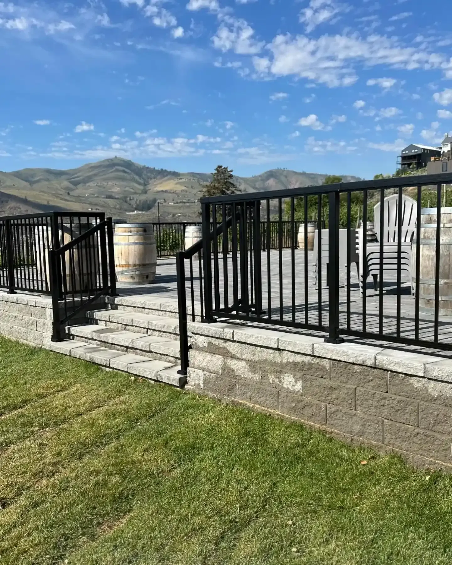 Stone patio with black railings, a lawn, and distant mountains under a partly cloudy blue sky