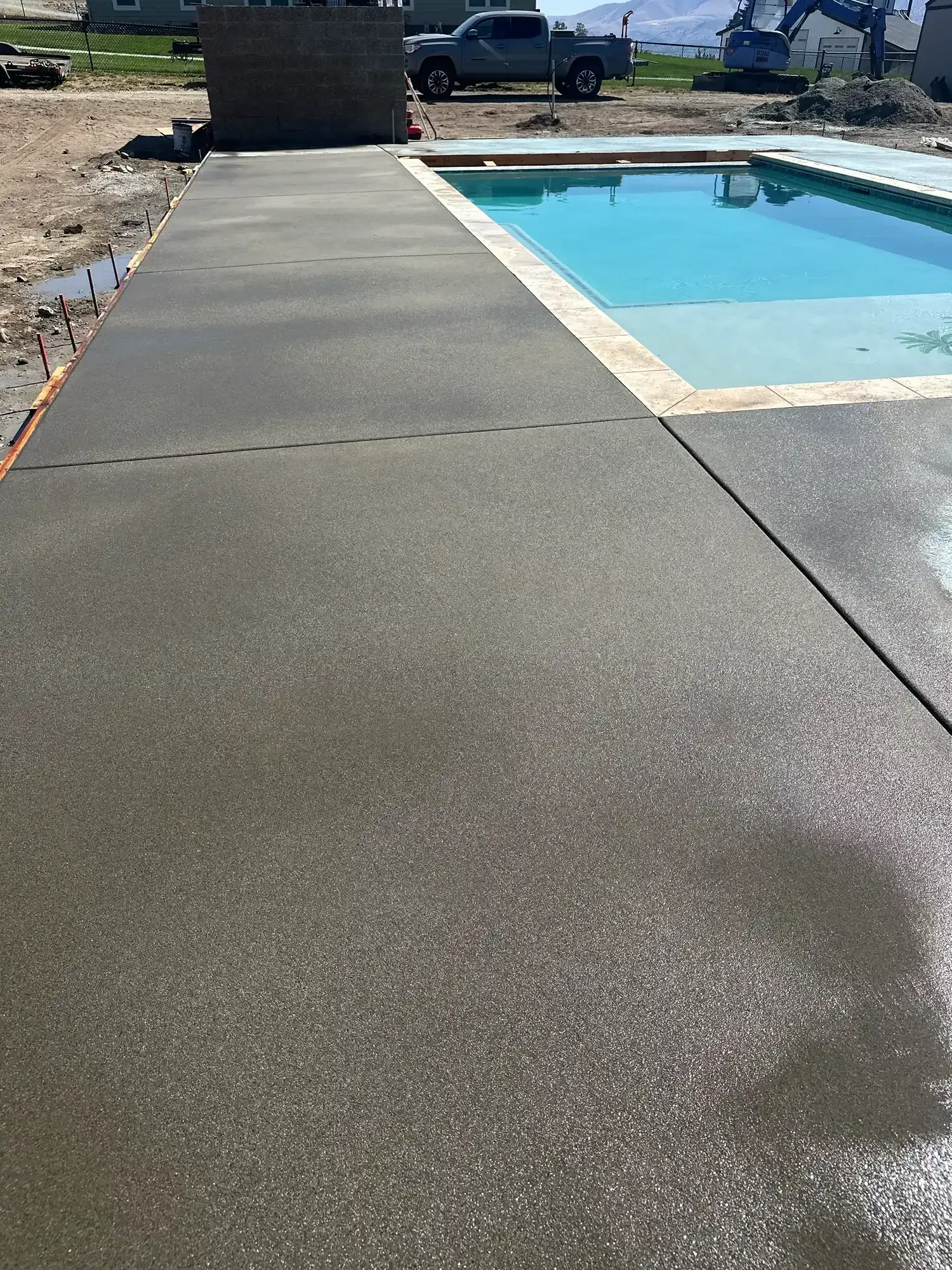 Concrete poolside walkway beside a turquoise swimming pool on a sunny day