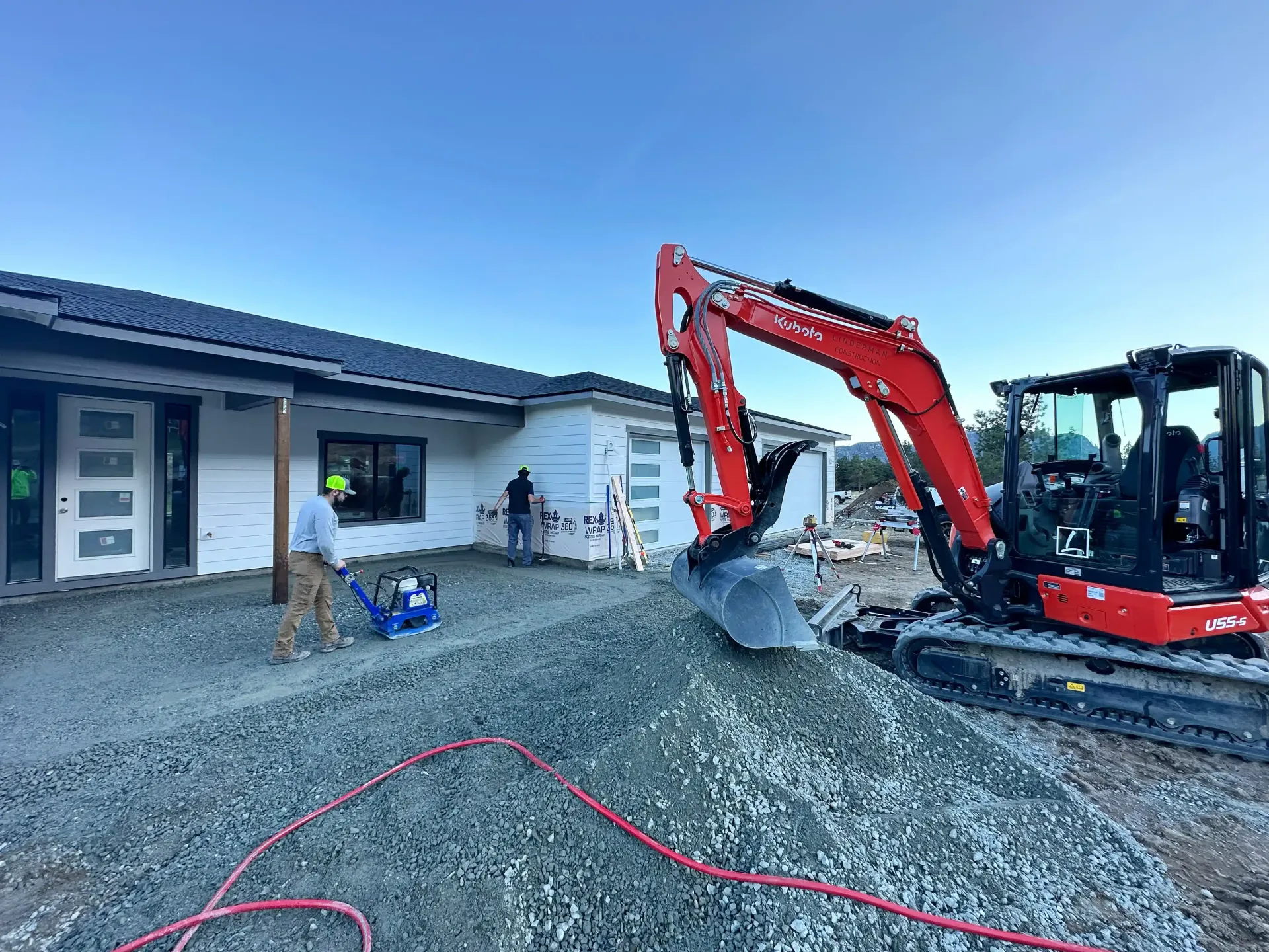 Red excavator moving gravel beside a house under construction