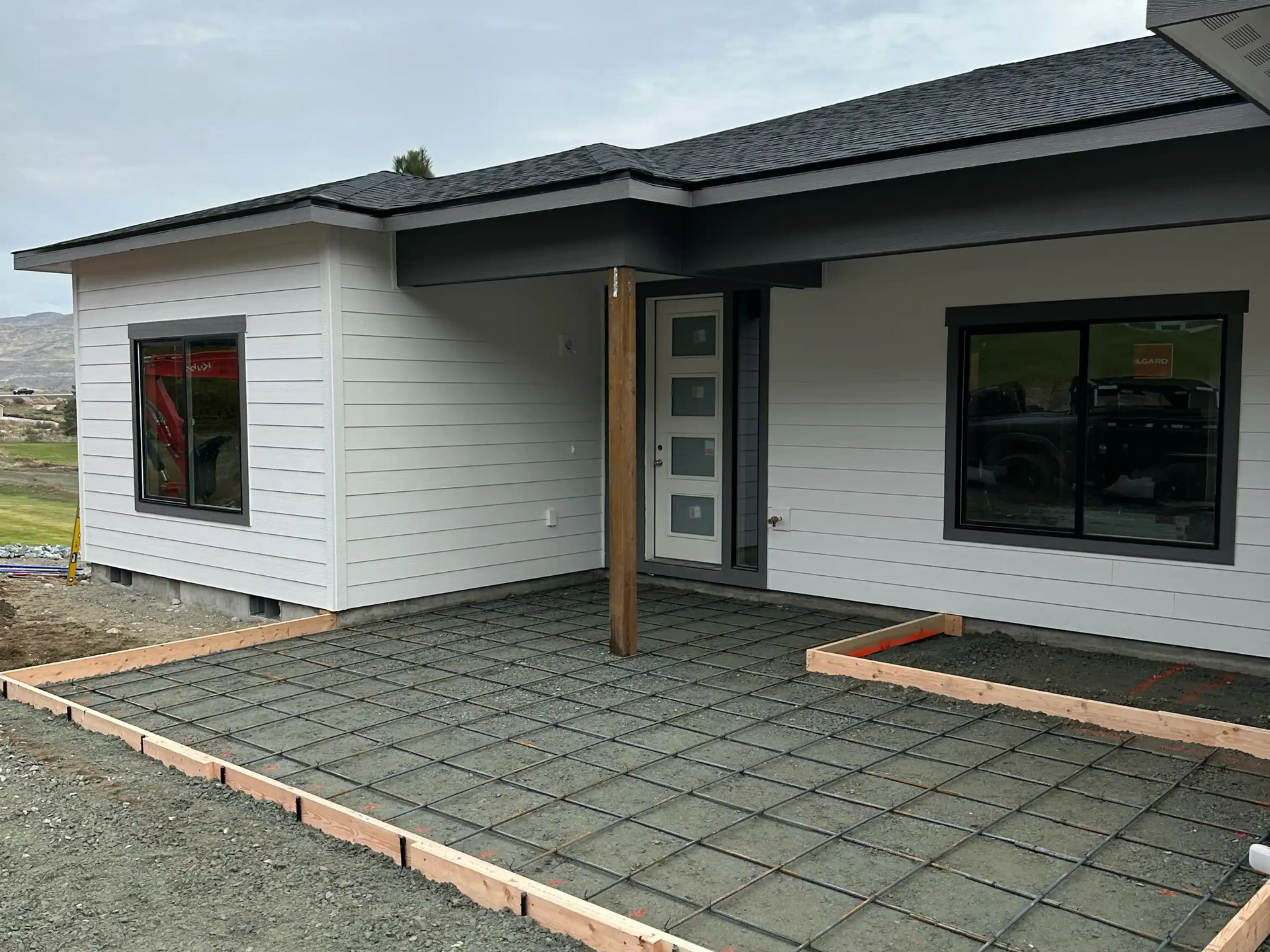 Modern single-story white house with a gray roof and paved front patio under construction