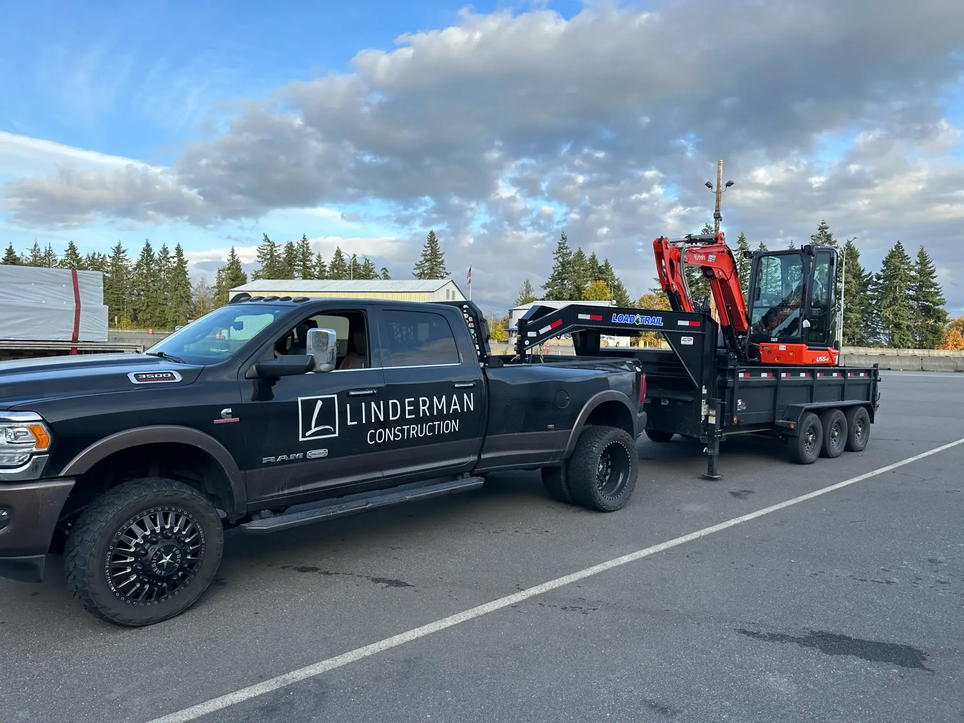 Black pickup truck towing a flatbed with red equipment on a roadside under a cloudy sky