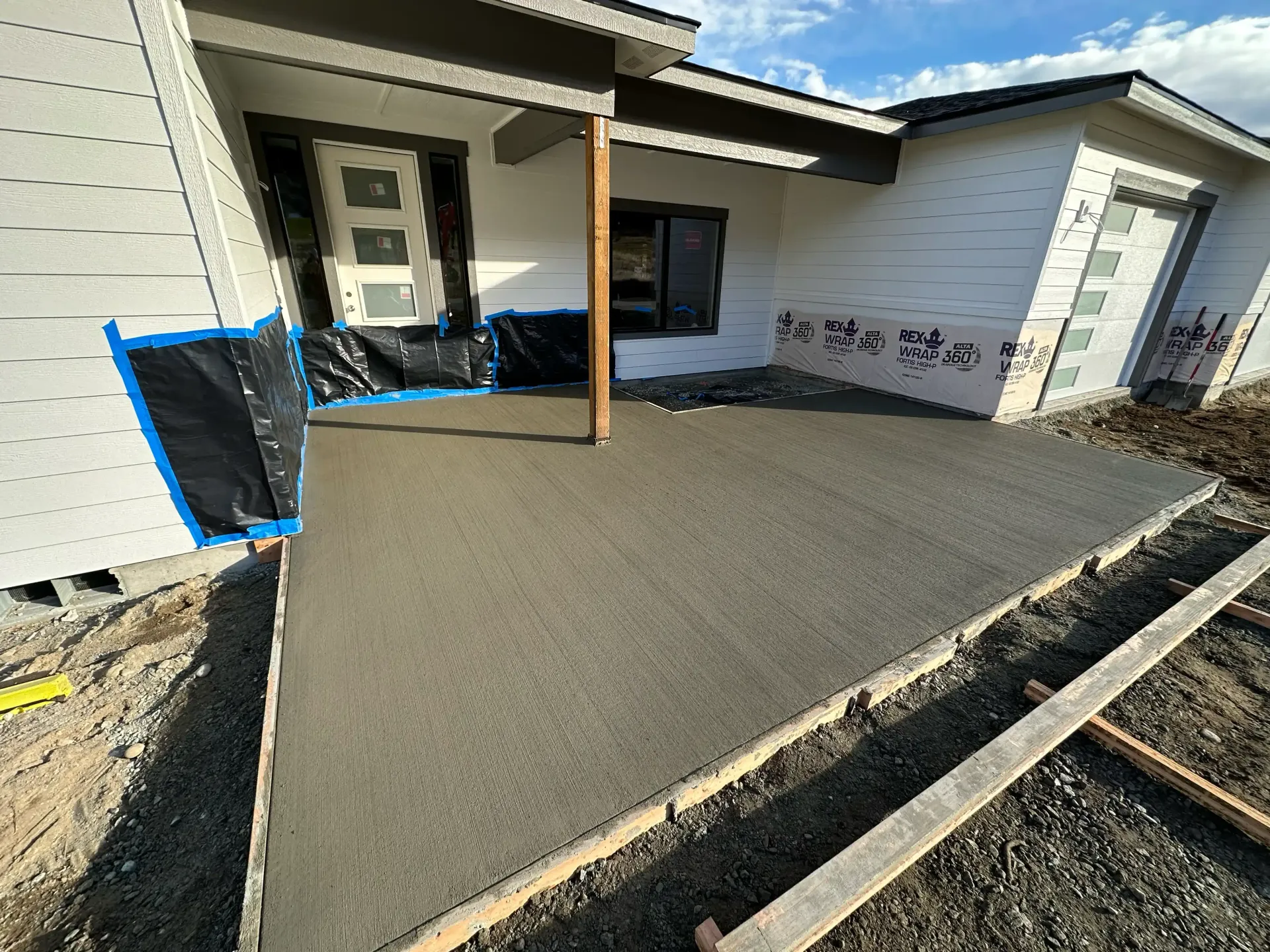 New concrete patio under construction beside a white house, with a ramp and temporary barriers.