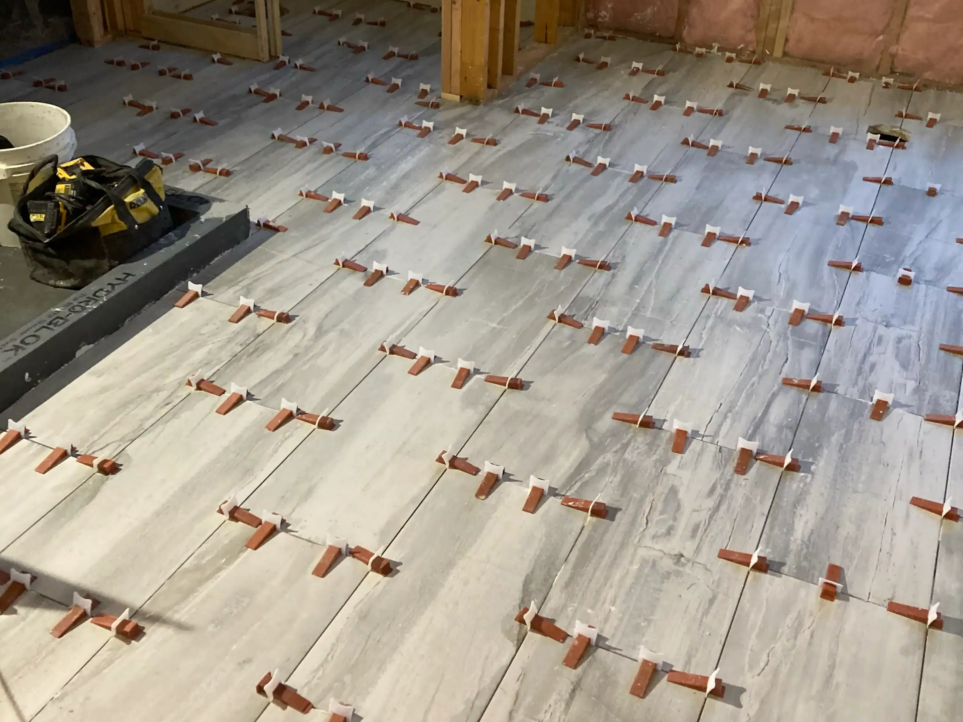 Partially tiled floor under construction with gray tiles and red spacers in a room framing area