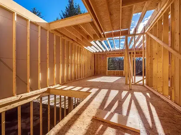 Framed wooden house interior under construction with sunlight through the roof trusses and wall studs