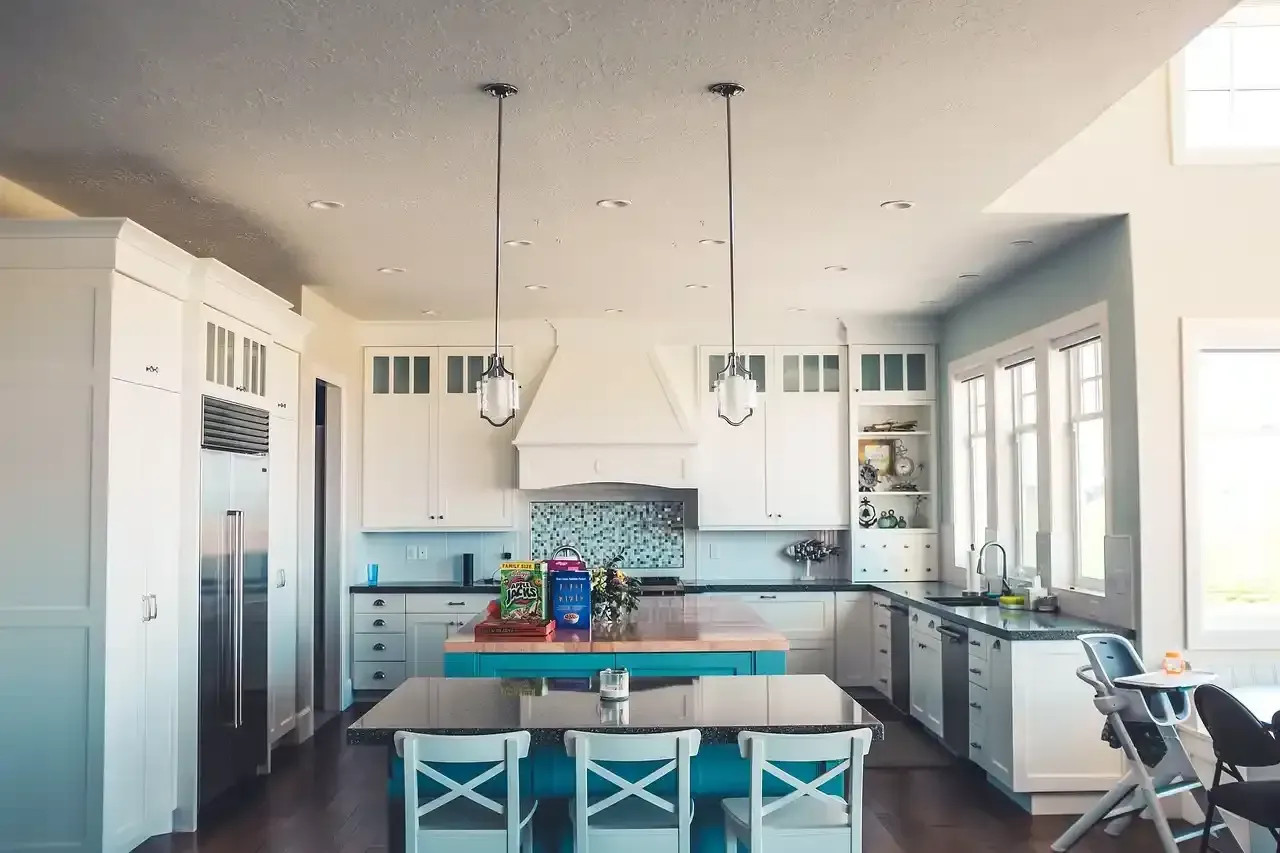 Bright modern kitchen with white cabinets, teal chairs, island, and large windows