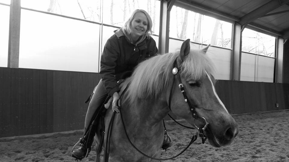 Persoon te paard in een overdekte rijhal, lachend naar de camera.