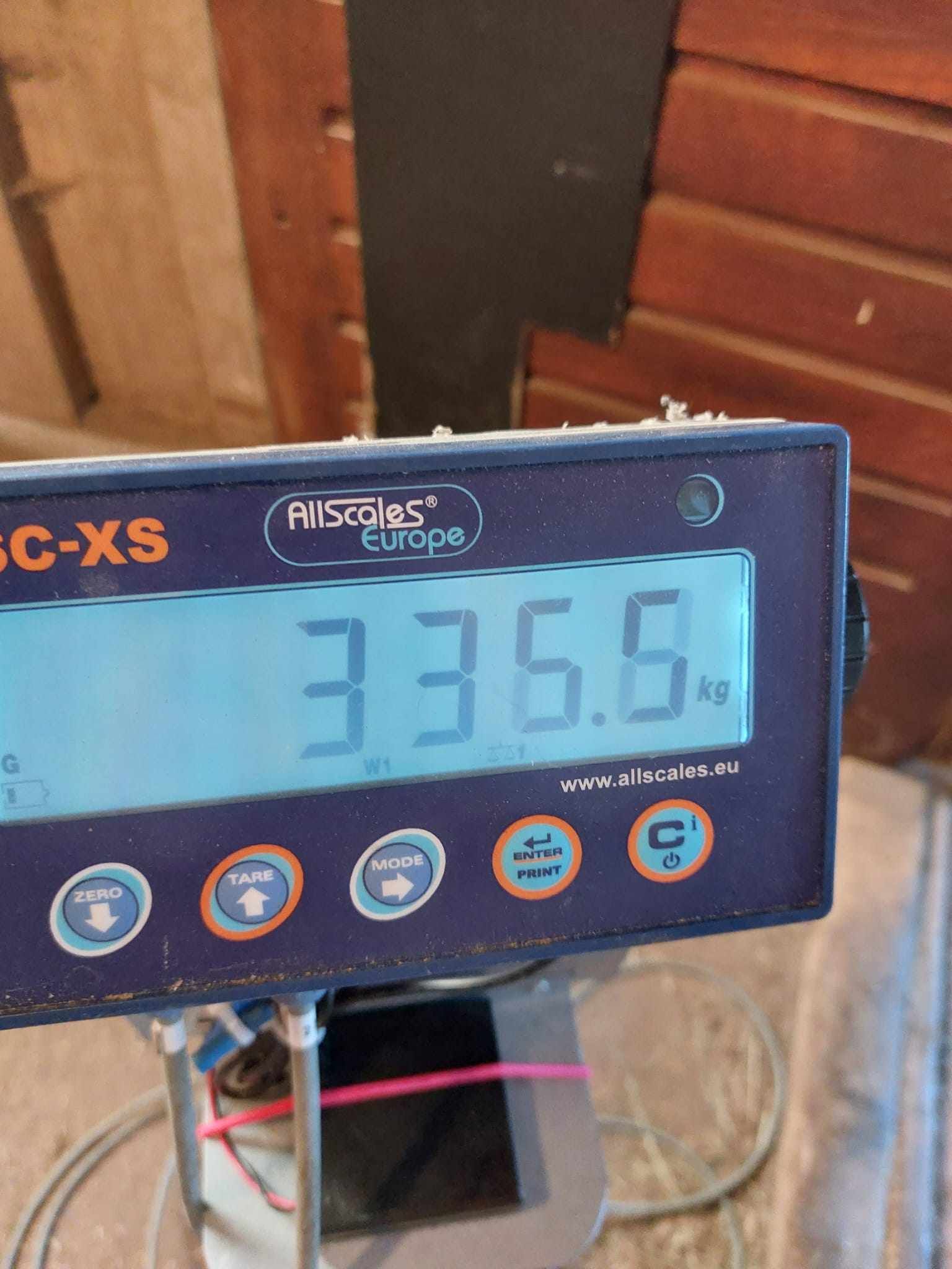 Digitale weegschaal met weergave van 33,56 kg op een blauw paneel in een houten kamer.