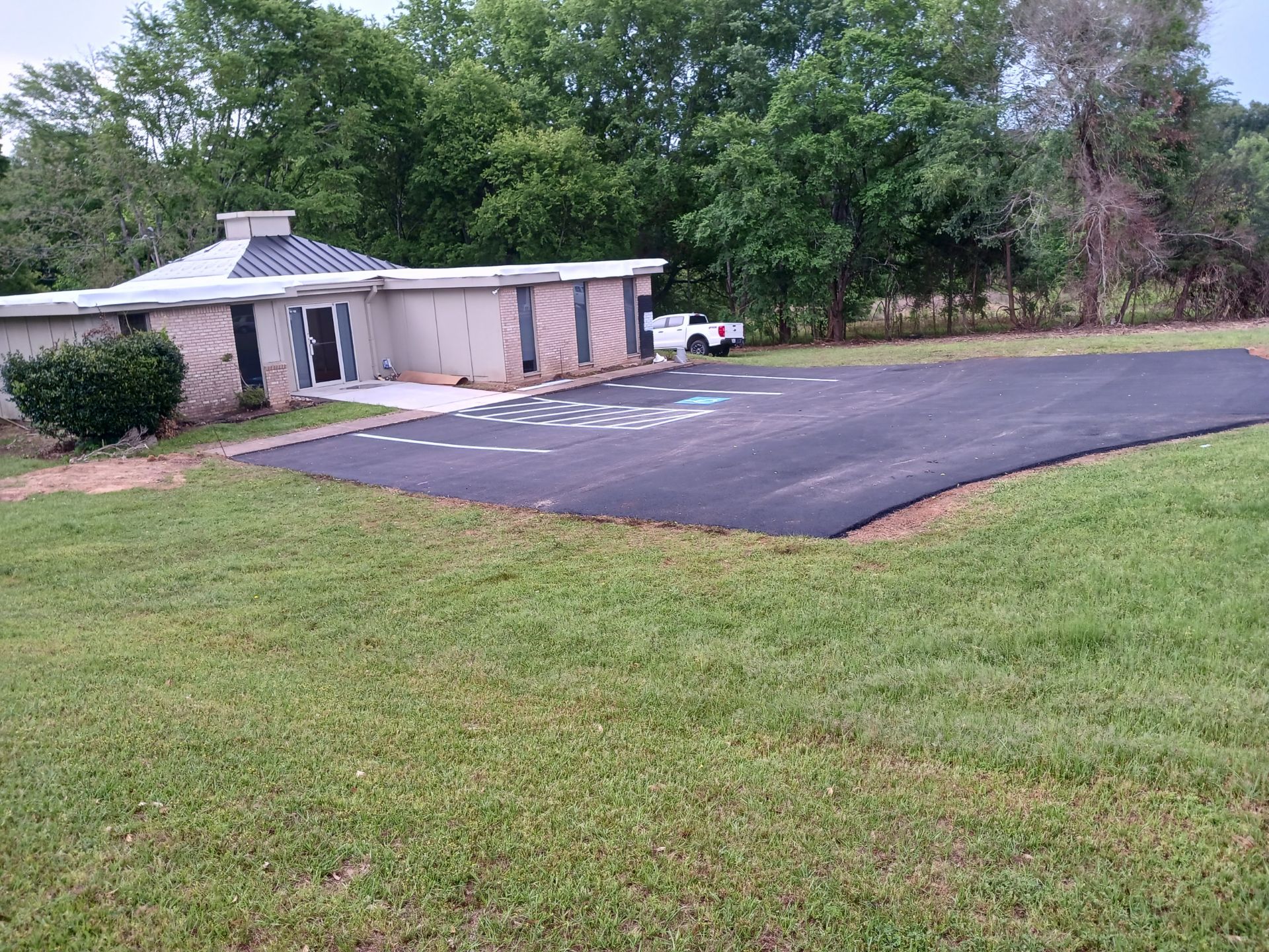 A house is sitting on top of a lush green field next to a parking lot