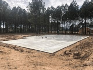 A large concrete slab is sitting in the middle of a dirt field surrounded by trees