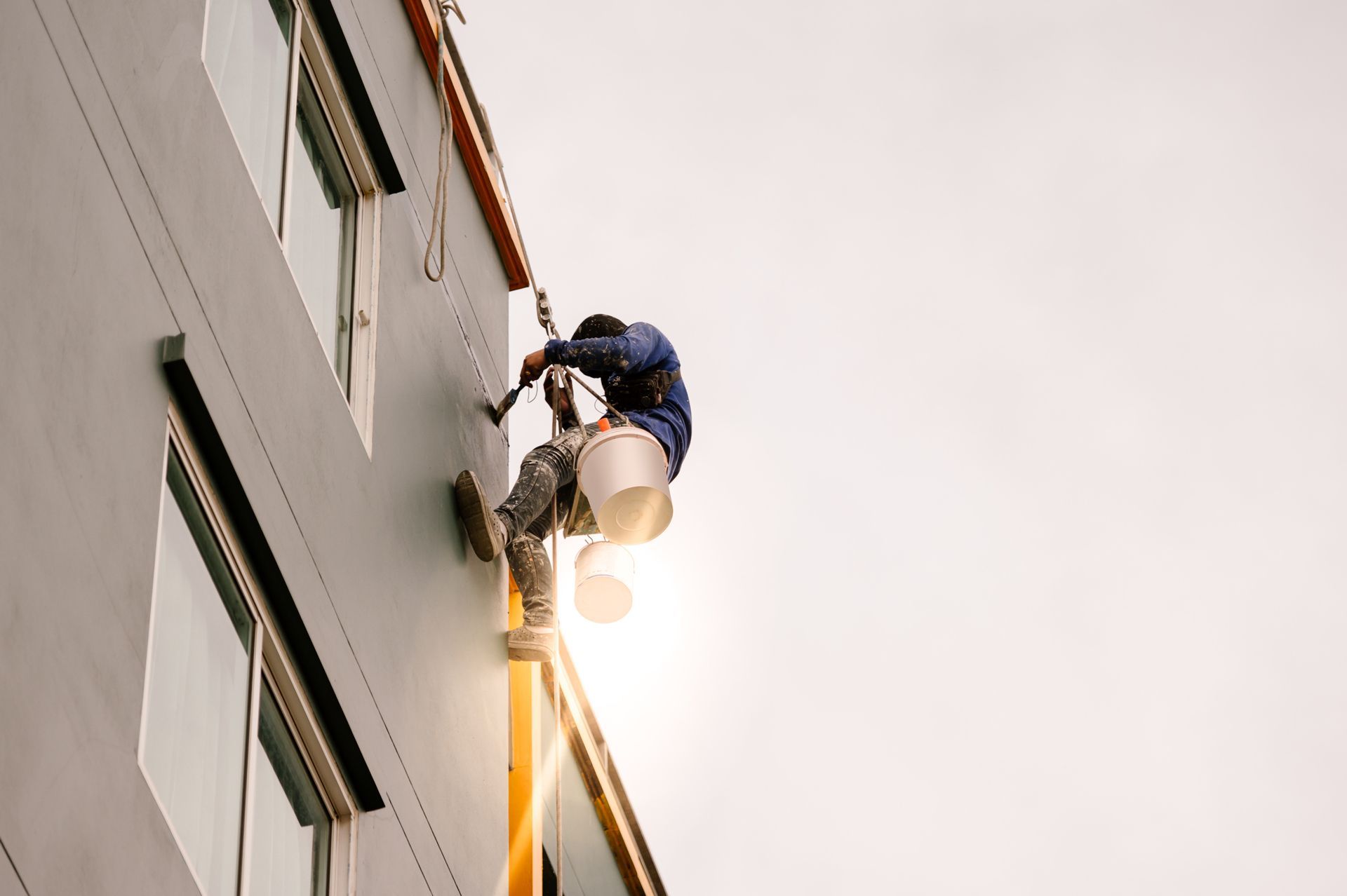 A Man is Painting the Side of a Building With a Bucket