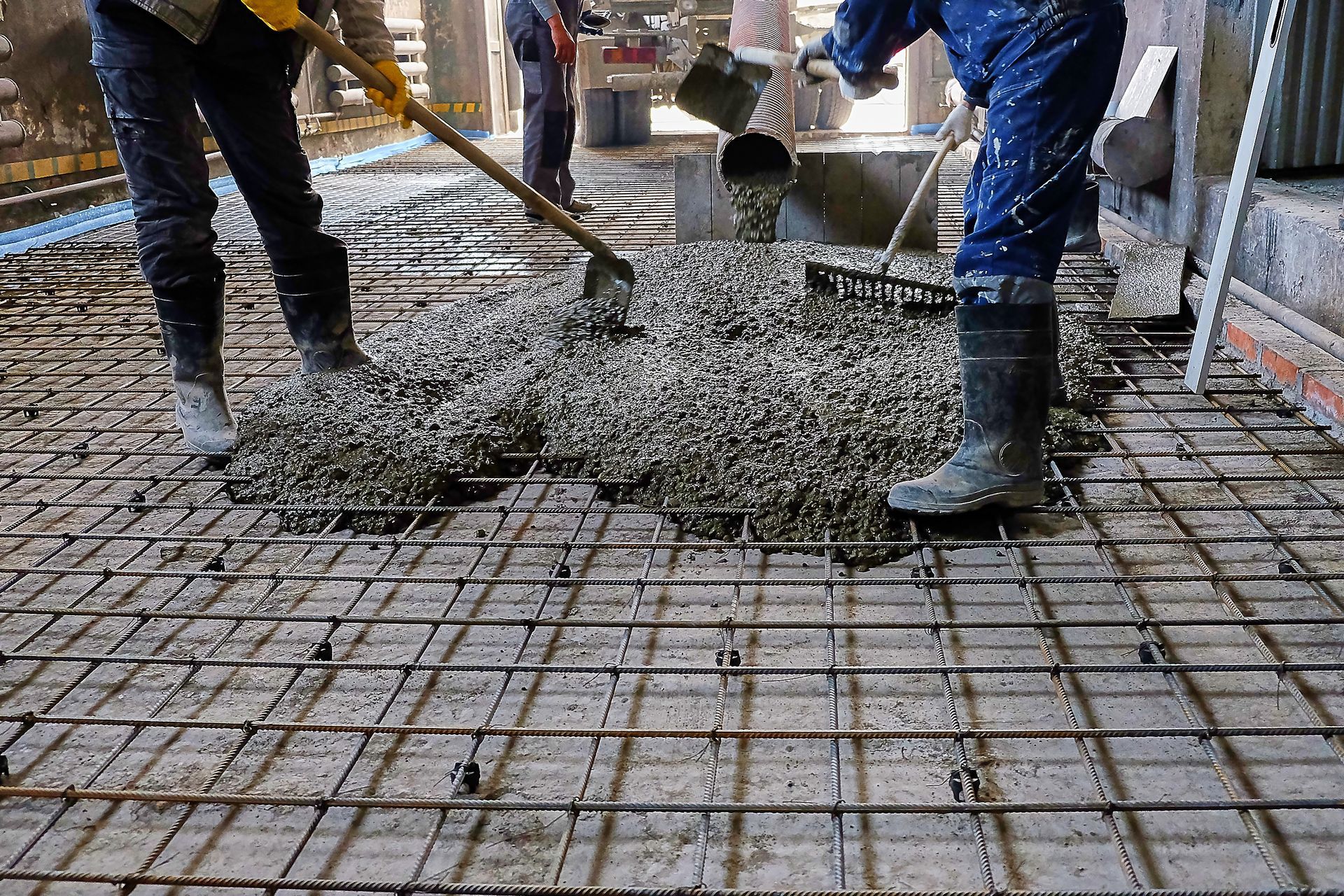 Two construction workers are pouring concrete into a grid.