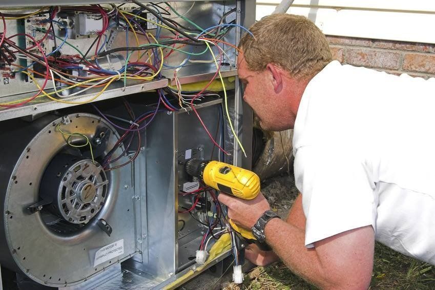 Man using a power drill on an HVAC unit, outdoor setting.