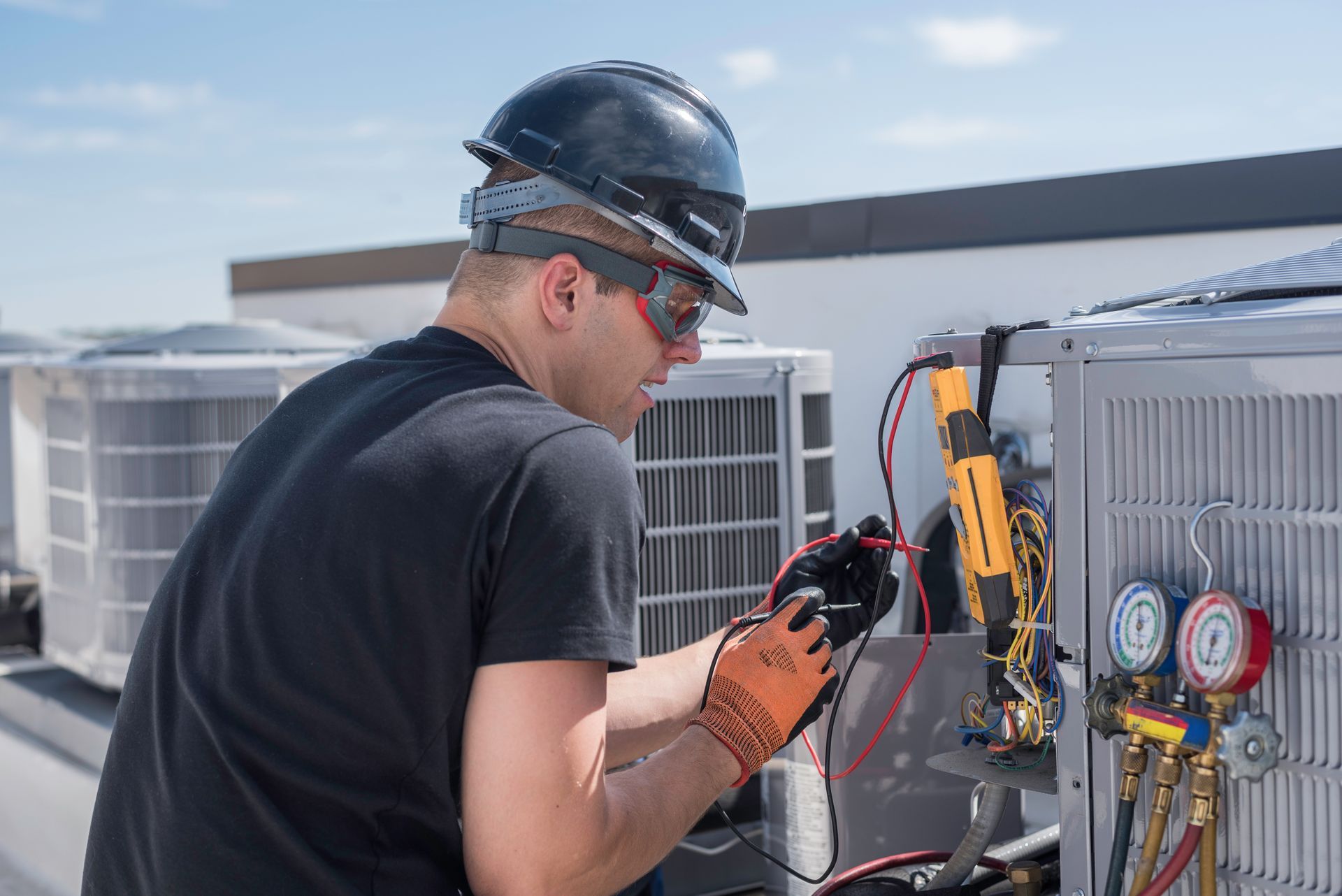 HVAC technician on a rooftop, inspecting air conditioning unit with gauges and tools.
