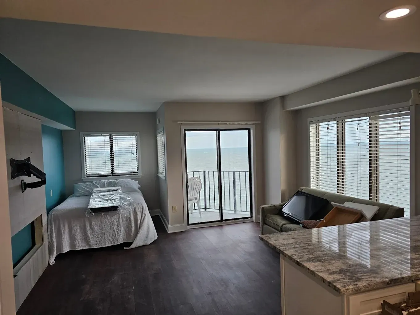 Studio apartment with ocean view, dark wood floor, small sofa, bed, sliding door to balcony, and a partial kitchen.