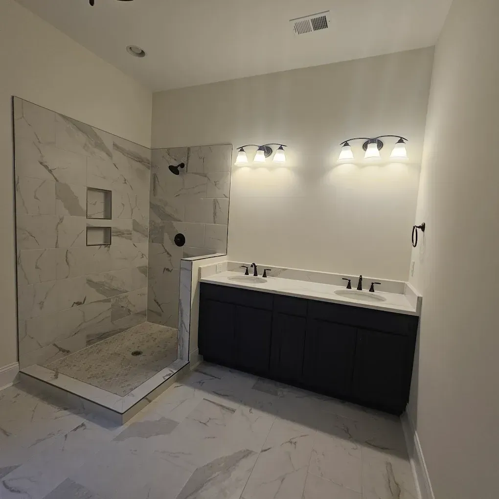 Modern bathroom with marble shower, double vanity, and dark blue cabinets.