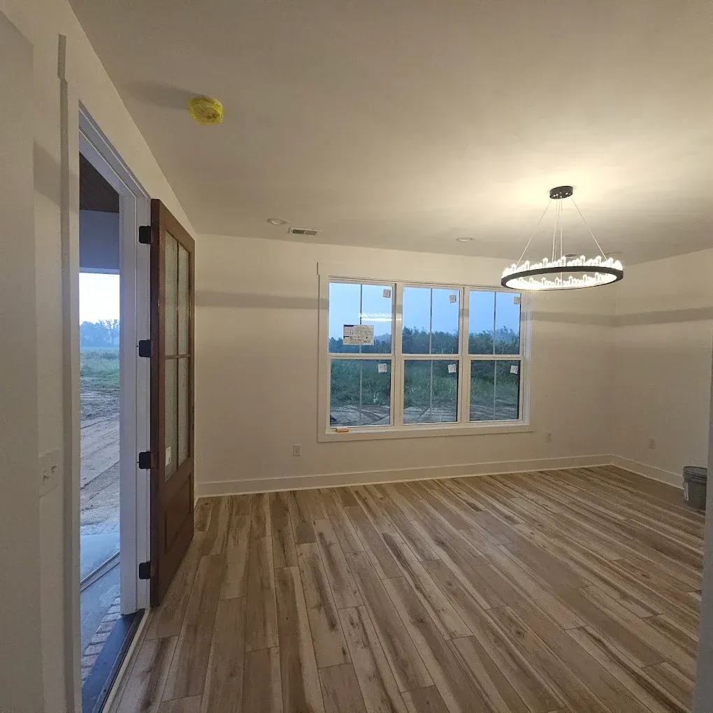 Narrow hallway with dark wood floors, white walls, and closed doors. A window is at the end of the hall.