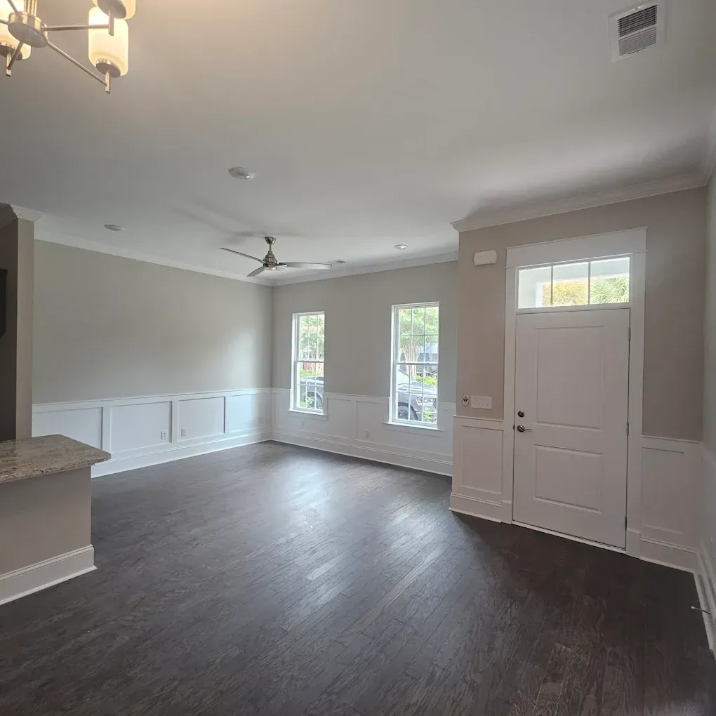 Empty living room with dark wood floors, white trim, and gray walls.