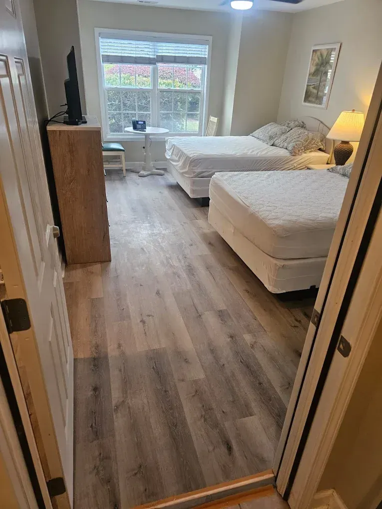 Bedroom with two beds, a window, dresser, and light-colored wood-look flooring.