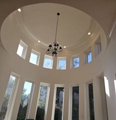 Interior view of a domed ceiling with multiple windows and a chandelier hanging in the center. White walls.